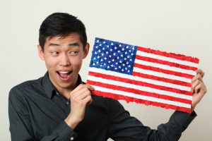Young Asian student showing US national flag and looking sideways