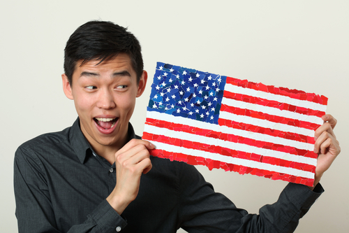 Young Asian student showing US national flag and looking sideways